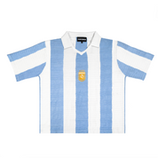 Front view of Argentina-inspired retro knit football shirt featuring vertical sky blue and white stripes, a white polo collar, and a gold embroidered crest.
