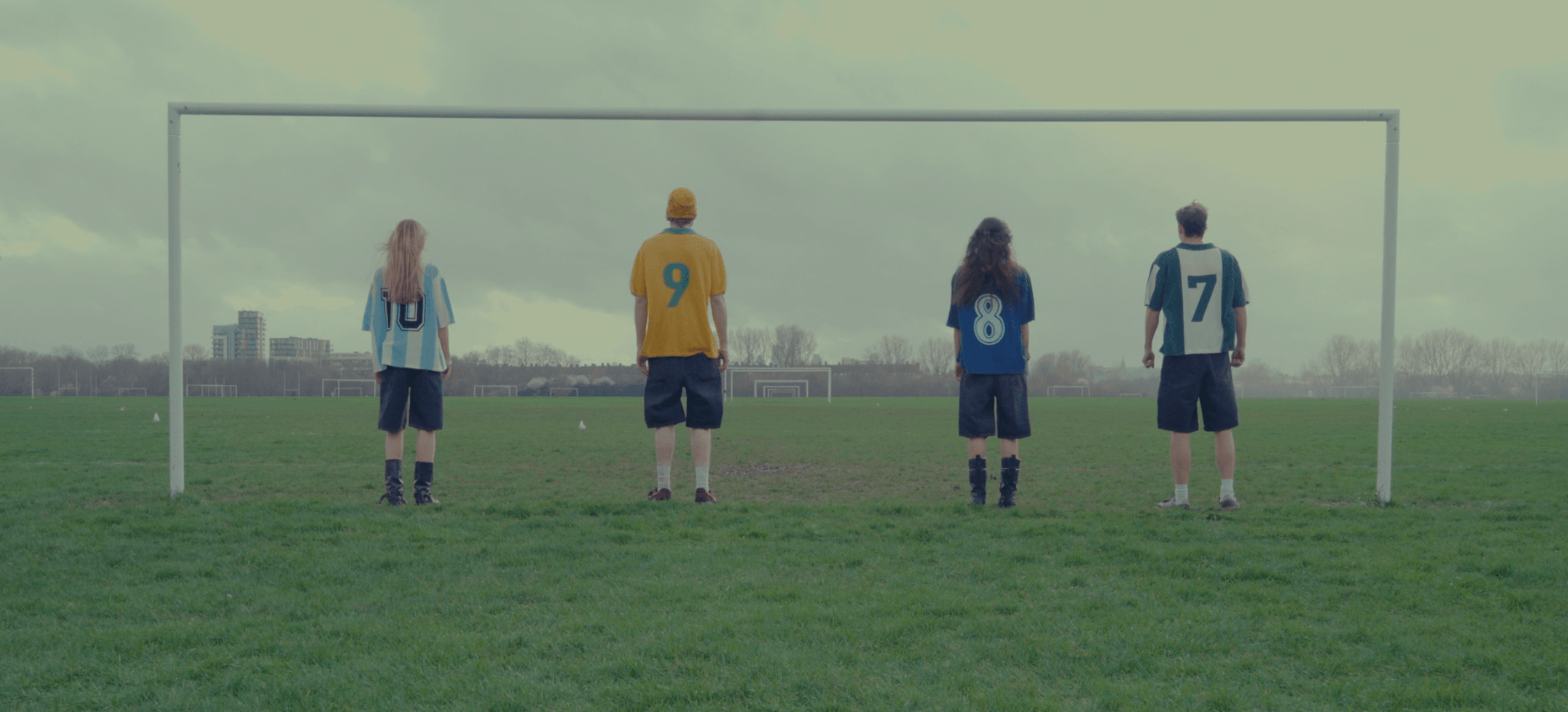 Four people in numbered jerseys standing on a green football pitch under a goalpost, representing the Parkzbus community,