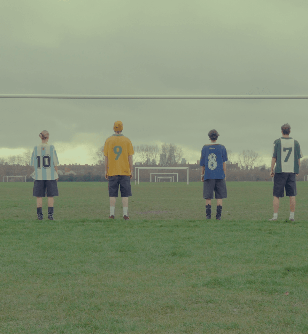 Group of people wearing Parkzbus retro knit football jerseys (Argentina, Brazil, Japan, and Nigeria styles) on a misty grass football field.